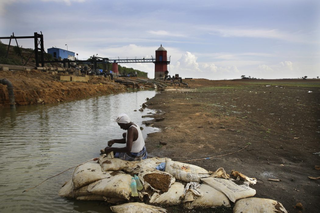 In this Wednesday, July 17, 2019, photo, an Indian fixes bait for fish, sitting on the dried up bed of Red Hills lake, a 4,500-acre 19th-century reservoir, in Chennai, capital of the Southern Indian state of Tamil Nadu. In Chennai, a coastal city of about 10 million and the capital of Tamil Nadu state, rapid development and rampant construction have overtaxed a once-abundant natural water supply, forcing the government to spend huge sums to desalinate sea water, bring water by train from hundreds of kilometers (miles) away and deploy an army of water trucks to people whose household taps have suddenly run dry. (AP Photo/Manish Swarup) Indien växer och med det följer vattenbrist