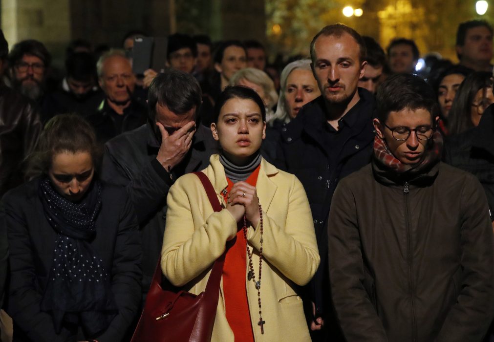People pray as Notre Dame cathedral burns in Paris, Monday, April 15, 2019. Massive plumes of yellow brown smoke is filling the air above Notre Dame Cathedral and ash is falling on tourists and others around the island that marks the center of Paris. (AP Photo/Christophe Ena) En betraktare knäpper händerna framför Notre-Dame i Paris