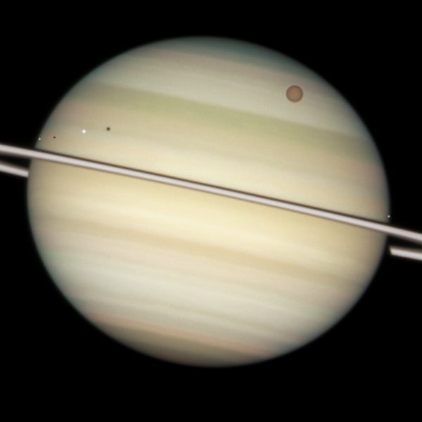 På denna bild tagen av Hubble-teleskopet syns flera av Saturnus månar passera framför den i bild.