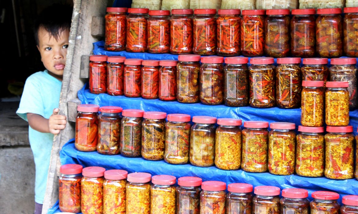 En pojke som tillhör khasifolket tittar fram bakom ett rikt utbud av inlagd chili, bambuskott, vilda frukter och bär som hans mamma säljer vid den väg som löper mellan de nordöstra delstaterna Assam och Meghalaya