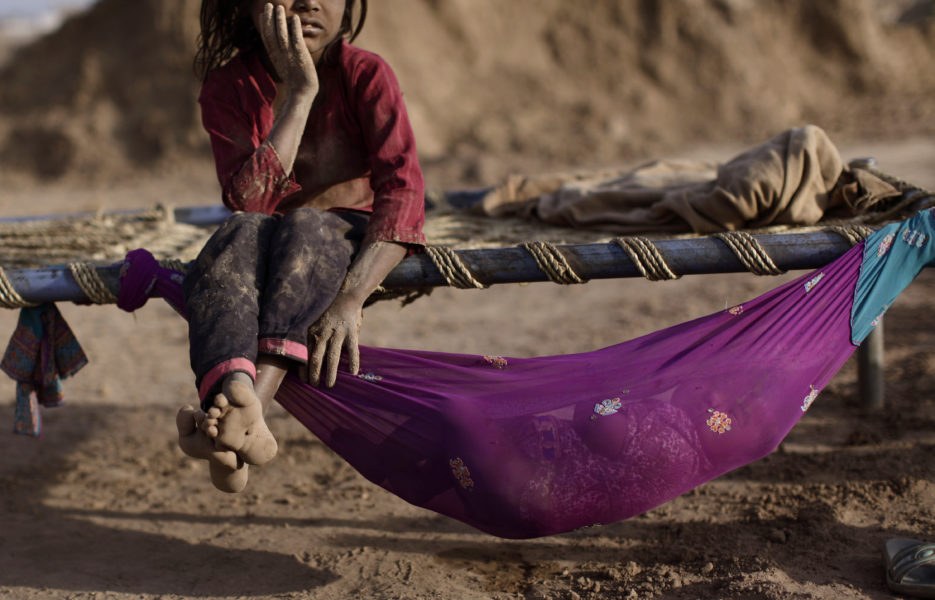 En femårig pakistansk flicka som arbetar i en tegelfabrik vilar lite.