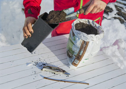 En person fyller en kruka med jord från en påse.