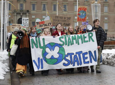 Ungdomar i organisationen Aurora klimatdemonstrerar med ett stort plakat med texten "Nu stämmer vi staten".