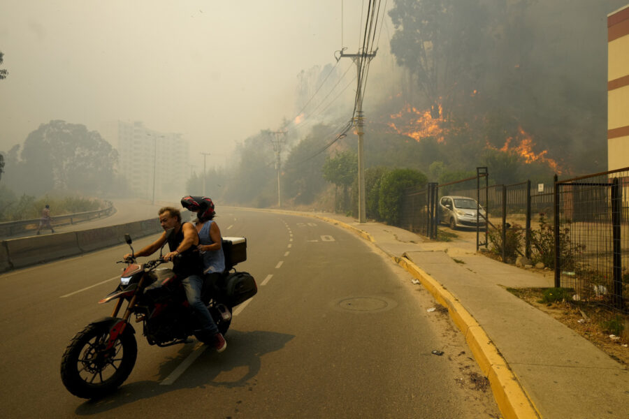 Två personer på en motorcykel rör sig bort från en skogsbrand.