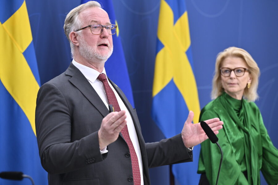 Johan Pehrson talar gestikulerande mot en bakgrund av svenska flaggor. I bakgrunden syns Elisabeth Svantesson.