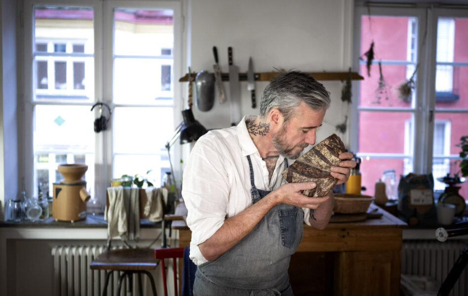 Bagaren Sébastien Boudet står mitt i ett kök och luktar på ett nybakat bröd.