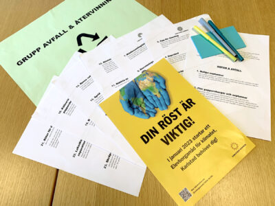 Workshopmaterial i en hög, överst en flyer med texten Din röst är viktig och två händer målade som en karta över jorden.
