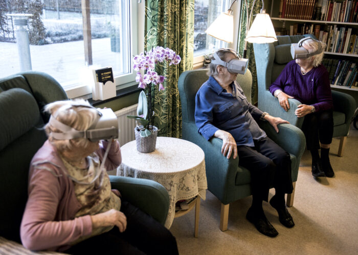 Tre personer på ett äldreboende sitter i fåtöljer med VR-glasögon.