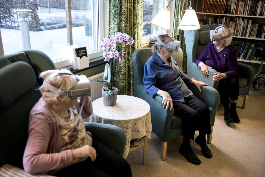 Tre personer på ett äldreboende sitter i fåtöljer med VR-glasögon.