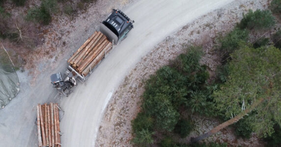 Fullastad timmerbil på barrskogskantad väg sedd från ovan.