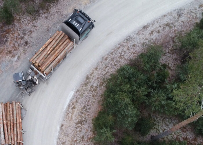 Fullastad timmerbil på barrskogskantad väg sedd från ovan.