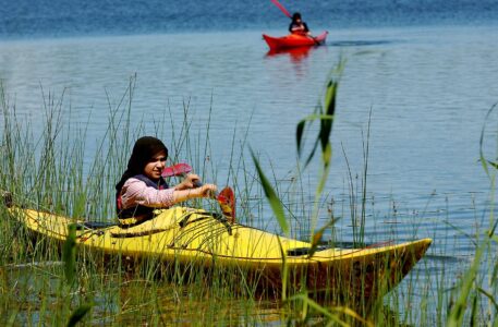 Ung kvinna paddlar kajak genom vass. i bakgrunden syns ytterligare en kajak.