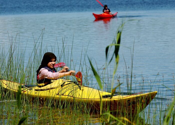 Ung kvinna paddlar kajak genom vass. i bakgrunden syns ytterligare en kajak.