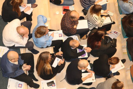 Människor med anteckningsblock i knät sitter på fyra rader, sedda ovanifrån.