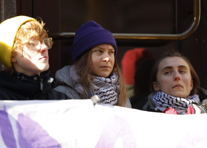 Tre aktivister, däribland Greta Thunberg sitter utanför Riksdagens port med ett plakat.