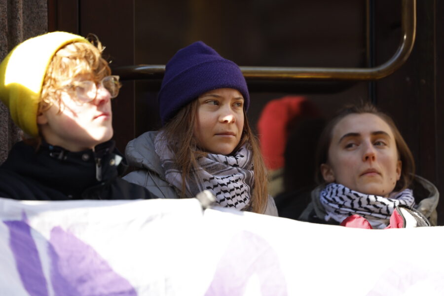 Tre aktivister, däribland Greta Thunberg sitter utanför Riksdagens port med ett plakat.