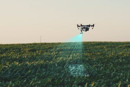 Drönare flyger över ett grönt fält och riktar blått ljus nedåt på grödorna.