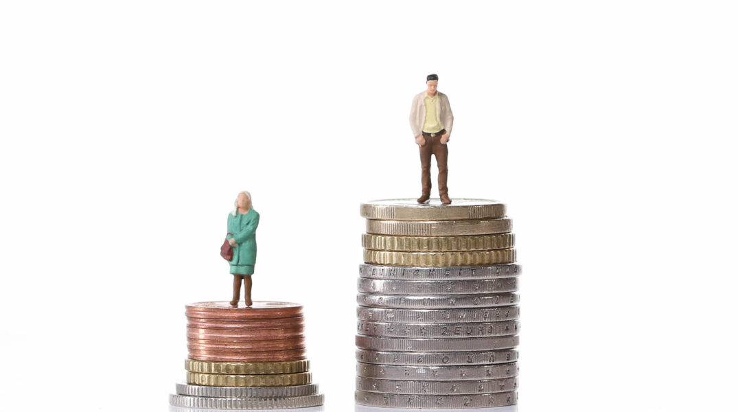Miniatyrdocka av kvinna står på låg stapel av mynt och mansdocka står på en hög stapel.