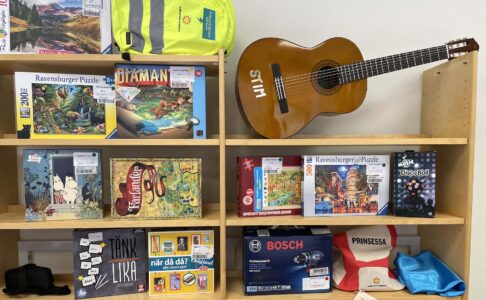 Hylla med spel, gitarr, tygpåsar med mera.