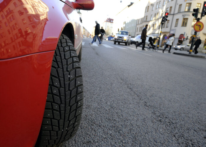 Närbild på dubbdäck på en röd bil, i bakgrunden en stadsgata.