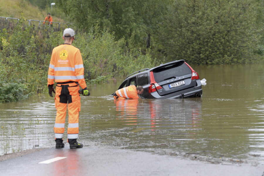 En man i orange varselkläder betraktar en annan man som undersöker en Volvo halvt under vatten.