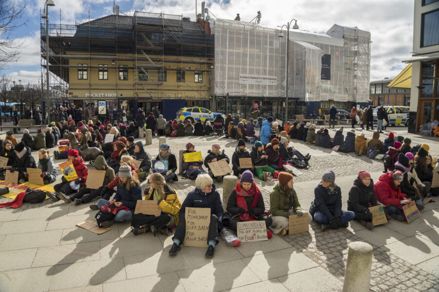 Klimataktivister sitter på marken i en ring med skyltar.