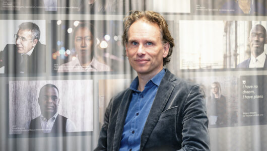 Porträtt av John Stauffer som tittar in i kameran, framför ett tunt draperi och med foton i bakgrunden.