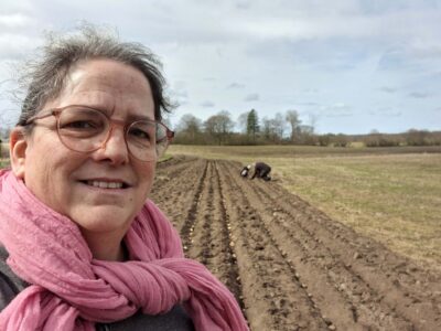 Kvinna med rosa sjal står framför mark där potatis just sätts.