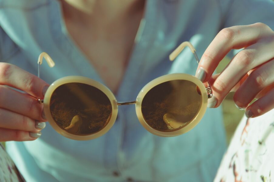 Turkosklädd kvinna håller ett par begagnade solglasögon i händerna.
