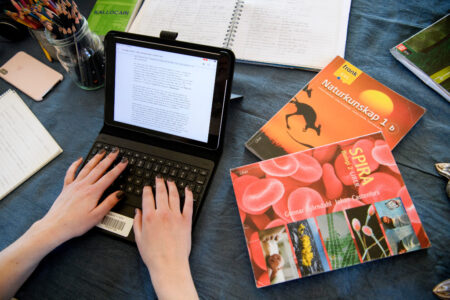 Händer på en dators tangentbord, samt ett par böcker.