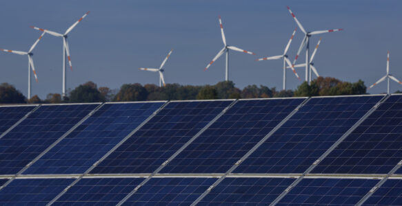 Ett gäng vindkraftverk mot blå himmel, i förgrunden solpaneler.