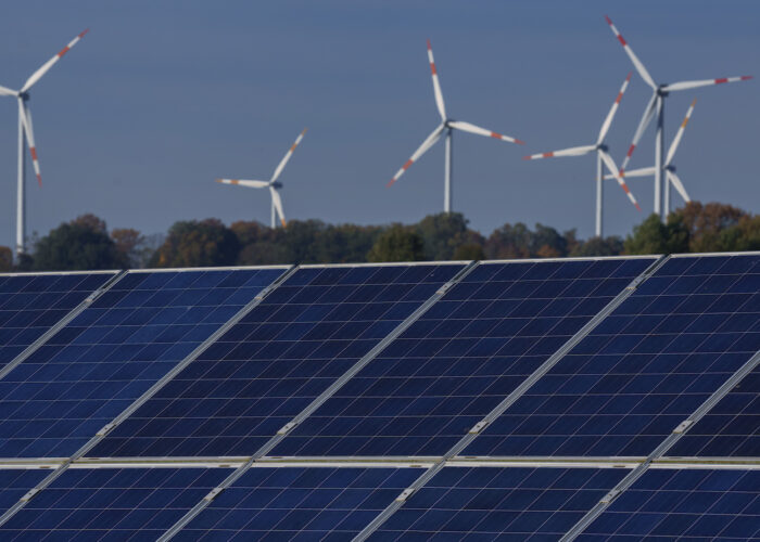 Ett gäng vindkraftverk mot blå himmel, i förgrunden solpaneler.