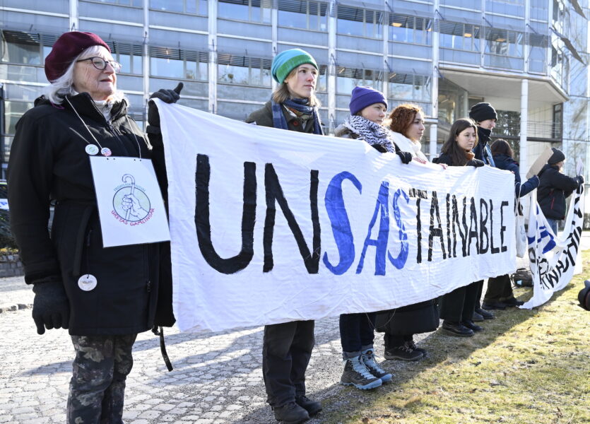 Demonstranter utanför SAS bolagsstämma, däribland Greta Thunberg, håller en vit banderoll med ordet UNSASTAINABLE på.