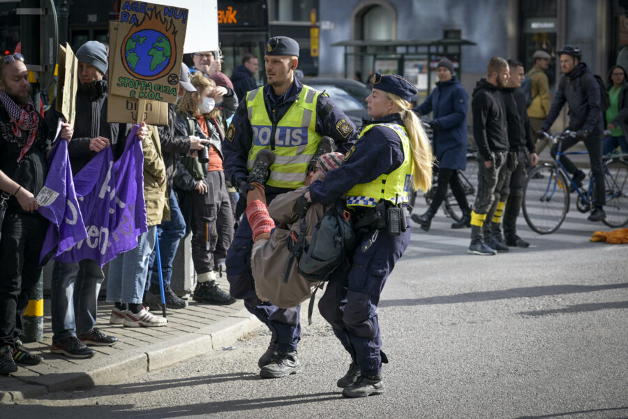Två poliser bär bort en klimataktivist från en demonstration.