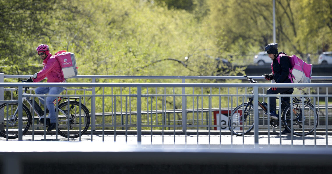 Två cykelbud på en bro, i bakgrunden gröna trädkronor.