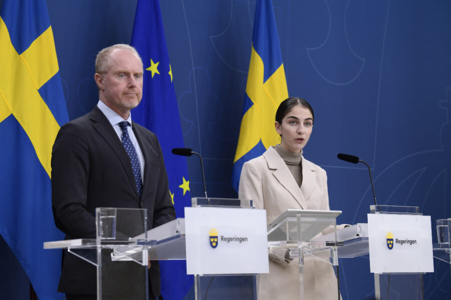 En man och en kvinna står framför svenska flaggan liksom en EU-flagga.