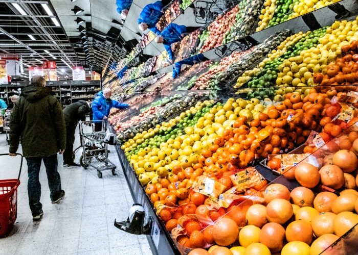 Kunder vid en frukt- och grönthylla i en stor matbutik.