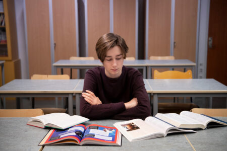 Elev sitter i skolbänk i ett klassrum med läroböcker framför sig.