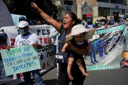 Kvinnlig demonstrant håller ett barn på ena armen framför plakat och banderoller.