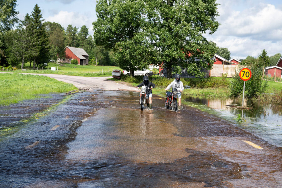 Två barn leder sina cyklar genom översvämmat område.