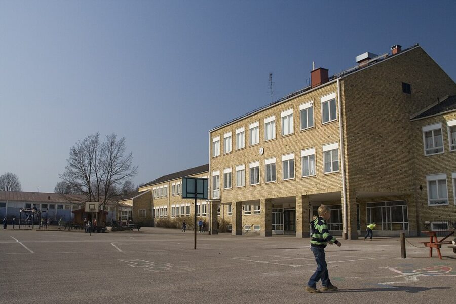 Asfalterad skolgård med gul tegelbyggnad.