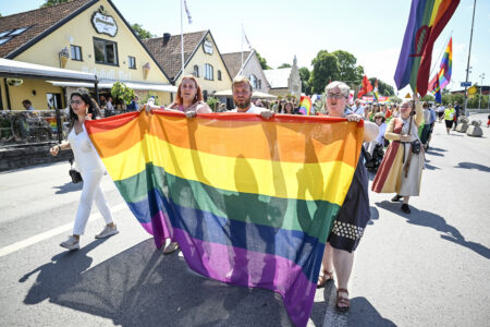 Personer går i parad och håller upp regnbågsflagga.