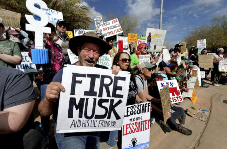 En folksamling där en man håller upp en skylt som det står Fire Musk på.