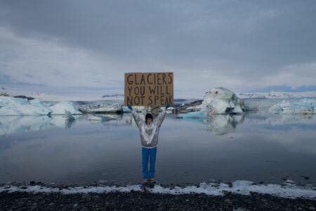 Person står på glaciär och håller upp en skylt.