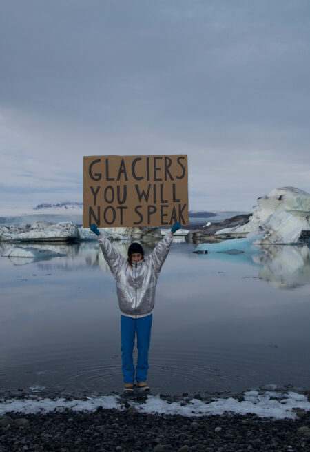 Person står på glaciär och håller upp en skylt.