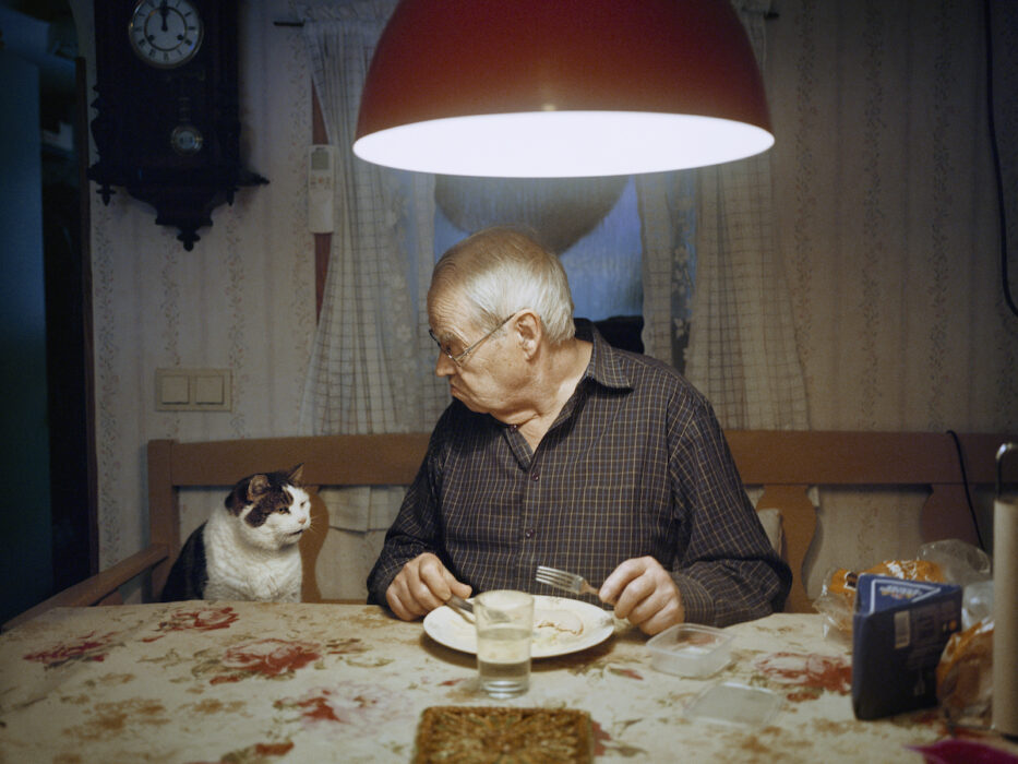 Gubbe med katt vid köksbord.