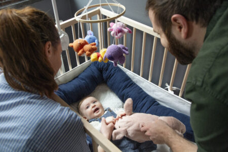 Föräldrar som hänger över en spjälsäng med en bebis i.