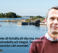 Jens Holm i skjorta och röd tröja med skärgården i bakgrunden.