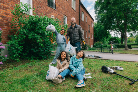 Tre barn och en man håller upp påsar av skräp de plockat.