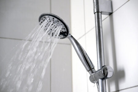 Duschmunstycke och vatten mot vitt kakel.